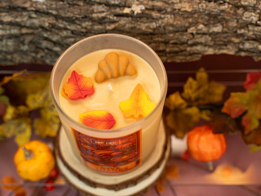 Candle with autumn-themed decorations in front of a tree and pumpkins