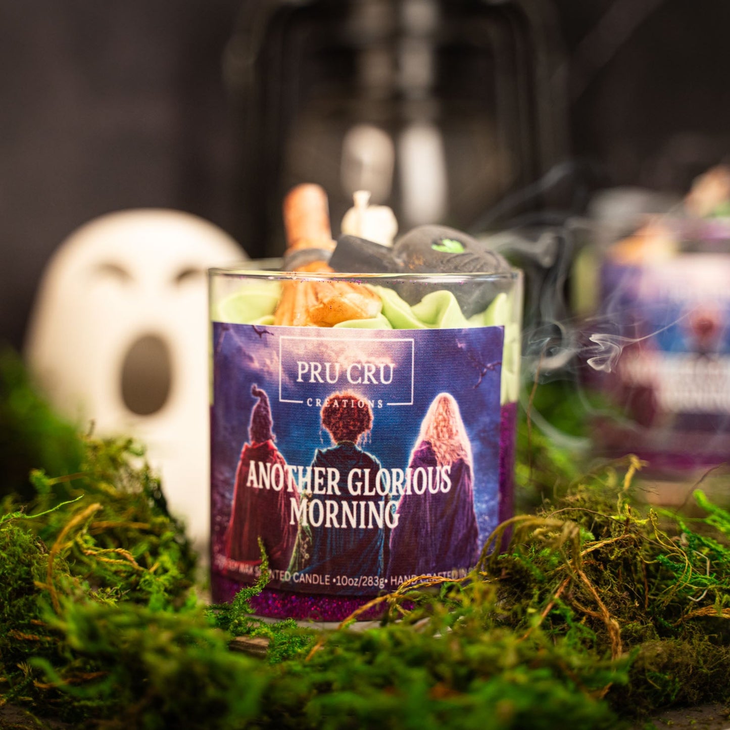 Candle with 'Pru Cru' packaging on a bed of moss, surrounded by similar candles.