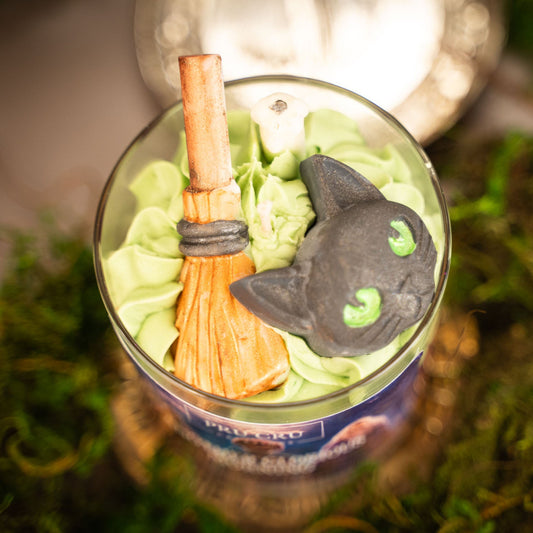 Decorative Halloween ornament with a broom and black cat on a bottle against a blurred background.