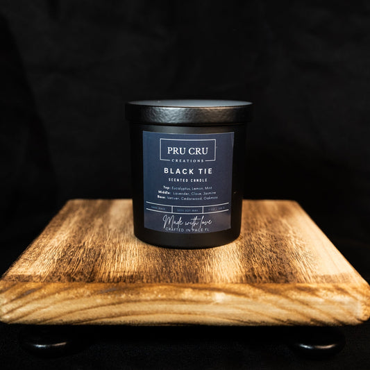 Pru Cru Black Tie candle on a wooden stand with a black background