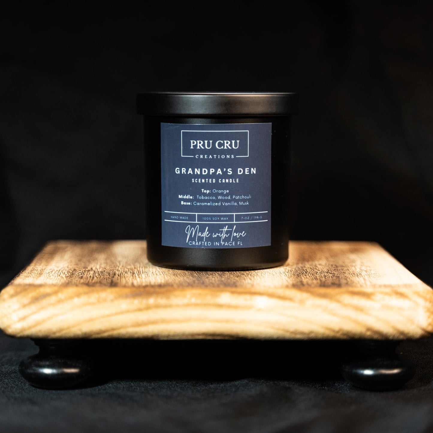 Black candle with a label on a wooden block against a black background
