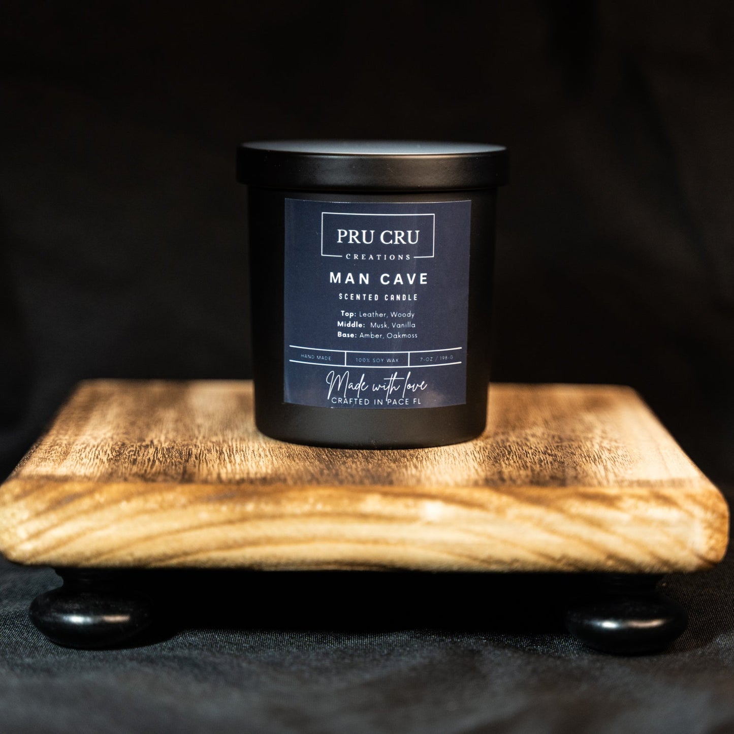 Black candle labeled 'Man Cave' by PRU CRO on a wooden stand with a dark background