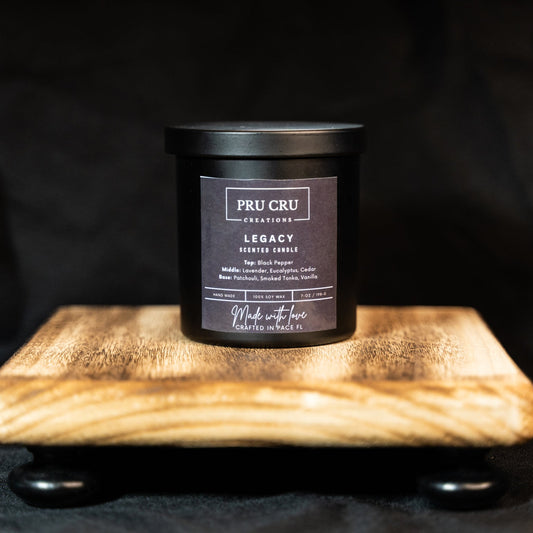 Black candle with a label on a wooden platform against a dark background
