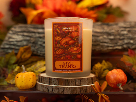 Candle with 'Give Thanks' label on a decorative stand with pumpkins and leaves