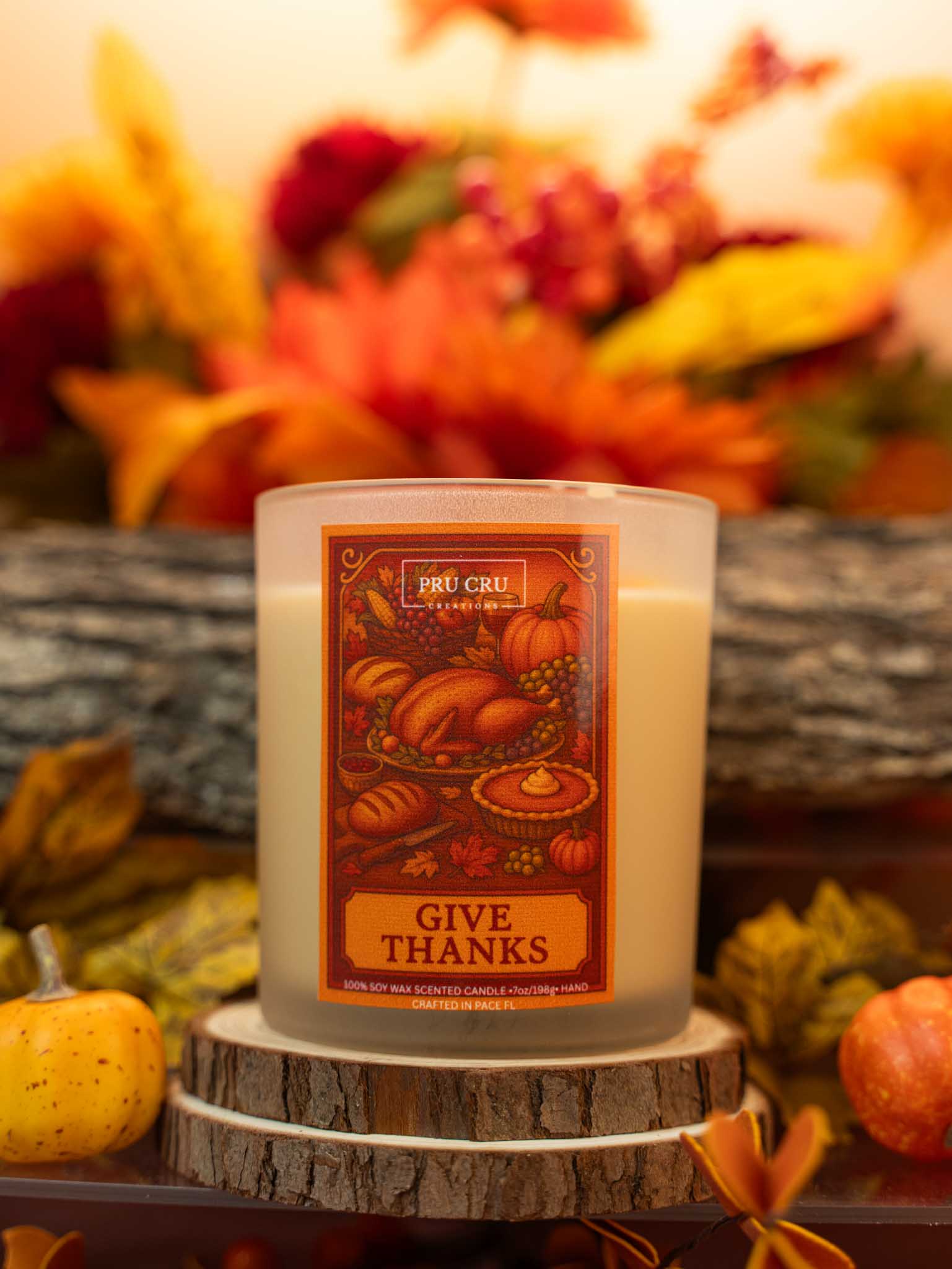 Candle with 'Give Thanks' label on a wooden stand with autumn decorations in the background