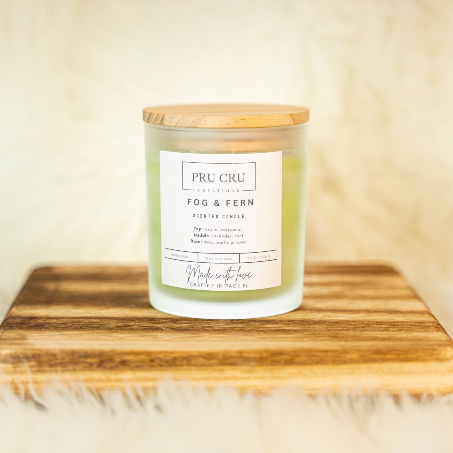 Candle labeled 'Pru Cru Fog & Fern' on a wooden surface with a soft background