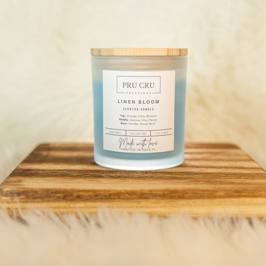 Candle labeled 'PRU CRU Linen Bloom' on a wooden board with a soft beige background